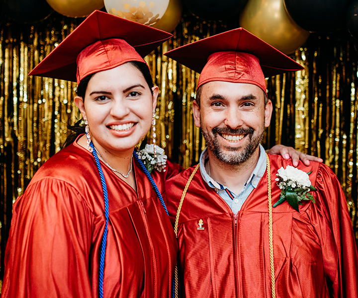 Student graduates wearing red caps and gowns, looking happy